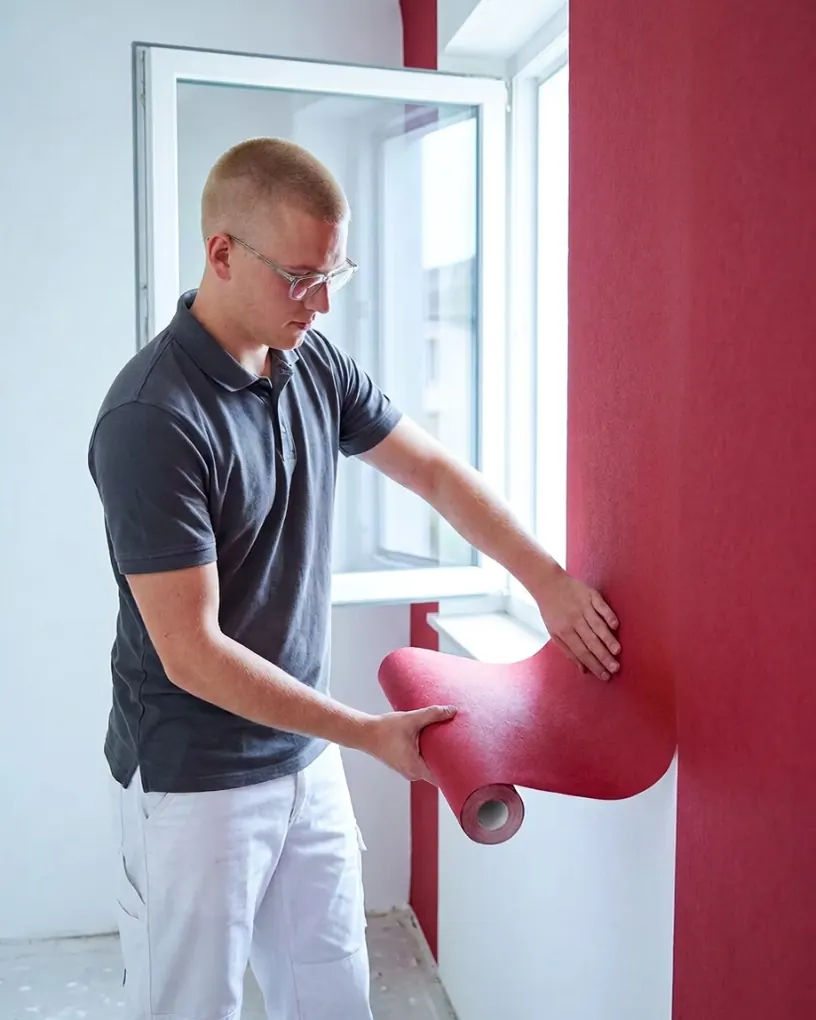 Maler tapeziert eine Wand mit roter Tapete in einer Wohnung in Fürth